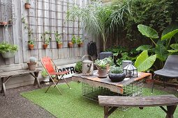 Old wooden bench and hand-made table in courtyard decorated with many potted plants and artificial grass rug