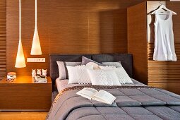 Elegant bed against wood-clad wall flanked by integrated bedside table and wardrobe