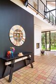 Colourful stag ornament on black table below round mirror on black wall in contemporary house with tiled and wooden floor