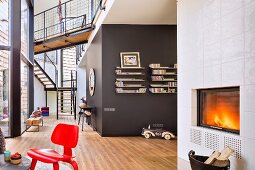 Red classic chair in front of fire in fireplace; brown-painted installation in background in open-plan, contemporary building