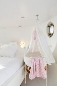 Cradle with canopy next to double bed in white bedroom of houseboat
