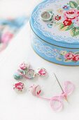 Romantic tin with pastel pattern of roses and lace, fabric-covered buttons and needle and thread