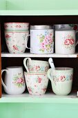 Romantic, vintage crockery with pattern of roses on pastel-green kitchen shelves