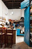 Küche mit Theke und Barhocker neben blau lackierten Schrank, im Hintergrund Mann