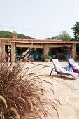 Finca terrace with roofed dining area, two loungers and grasses in foreground
