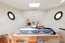 Custom bed on platform with porthole windows on either side in houseboat