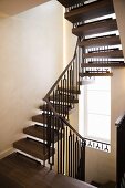 Winding metal staircase with wooden treads and handrail and tall stairwell window
