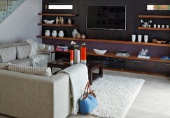 Elegante Loungeecke mit heller Sofagarnitur, gegenüber dunkelviolett getönte Wand mit Holzablagen und integriertem Flachbildfernseher