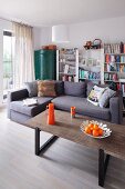 Coffee table with orange accessories, lilac-grey corner couch and simple bookcase in background