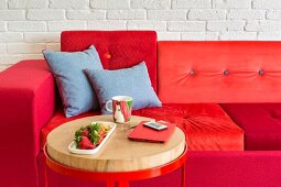 Sofa with cushions in various shades of red and side table with round metal frame and wooden top