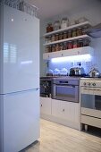 White fridge-freezer opposite kitchen counter and storage jars on wall-mounted shelves