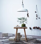 Small pine tree on wooden stool, presents wrapped in brown paper and mobile with pine cone pendants