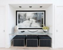 Large black and white picture in niche above glass shelf and black pouffes