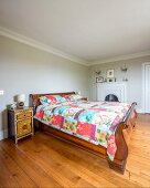 Elegantes, antikes Schlittenbett mit bunter Patchworkdecke und asiatisches Nachtkästchen in schlichtem Schlafzimmer
