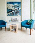 Blue fifties' armchairs flanking side table in front of artwork in narrow niche