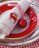 Rot-weisses Karoband mit Weihnachtskugel um bestickte Leinenserviette mit Hirschmotiv