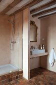 Wood-beamed ceiling, stone-tiled floor and partition between sink and shower areas in rustic bathroom