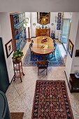 View down from gallery onto patterned rug and stone floor and dining area with antique, oval table in background in traditional interior