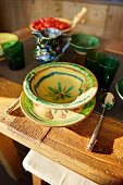 Gedeck mit bemalter Keramik und grünen Trinkbechern auf rustikalem Holztisch