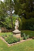 Antique stone statue on plinth in flowerbed in park belonging to Villa Cimbrone