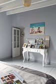 Schlafzimmer mit graublauem Dielenboden und Wänden, weißer Konsoltisch mit Bildern