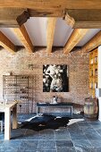 Wood-beamed ceiling, brick wall, large photo, bench and cowhide rug on slate floor in loft apartment