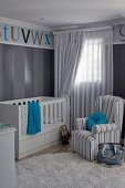 In Grautönen gestreifter Sessel vor Babybett in Kinderzimmer mit blauen Akzenten