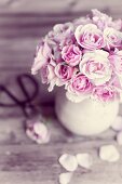 Ein Strauß rosa Rosen in Keramikkrug, daneben einzelne Blüte und Blütenblätter