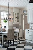 White and grey country-house kitchen with chequered floor and dining set below chandelier
