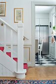 White-painted wooden staircase in hallway and open door with view of stainless steel fridge in kitchen