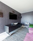 Black sideboard below flatscreen TV on grey and brown striped wallpaper in modern interior