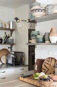 Edelstahlregal mit Geschirr an weiss getünchter Wand in einer Küche