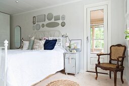 Antiker Armlehnstuhl in Zimmerecke neben Tür, seitlich Doppelbett mit weißem, schmiedeeisernem Gestell im Schlafzimmer