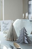 Aus bedruckten Buchseiten und schwarz-weißem Dekopapier gefaltete Weihnachtsbäume als Tischdeko für die Weihnachtszeit