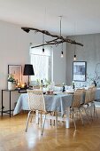 Festively set Christmas dining table with Scandinavian cane chairs and lights suspended from branch