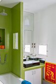 Washstand with base unit next to partition wall covered in green mosaic tiles
