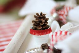 Pine cones in tiny white plant pots decorated with red ruffled trim