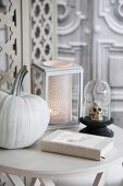Halloweendeko auf Tisch, weiss lasierter Kürbis, Deko Totenschädel unter Glashaube und romantisches Windlicht