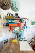 Wooden table below colourful boxes on bracket shelves and children's drawings on wall