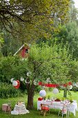 Set table in garden under white lanterns hung from tree for Swedish crayfish festival