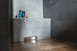 Ausschnitt einer bodenebenen, grau gefliesten Dusche, mit Wandablauf in schmaler Vormauerung, Badutensilien