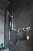 Duschbereich grau gefliest mit Handbrause an Duschstange und Armatur