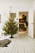 Geschmückter Weihnachtsbaum davor Tierfell auf weißem Dielenboden, im Hintergrund offene Tür mit Blick auf Luftballons und Bücherregal