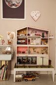 Dolls' house on stool below heart-shaped clock on wall