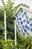 weiße Holz-Giebelfassade dekoriert mit blauen Wandtellern im Garten mit Deko-Holzpfählen