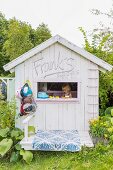Little girl playing in wooden play house with window in gable end in summery garden