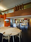 Blick über Essbereich in offene Designerküche, holzverkleideter Galeriebereich mit orangefarbener Wandscheibe