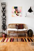 Patterned rug on wooden floor in front of cane couch with cushions next to ethnic sculpture hung on wall