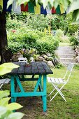 Rustic garden table with turquoise-painted frame and folding chairs in front of steps in garden