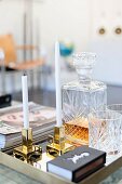 White candles in brass candlesticks next to crystal carafe and glasses on tray